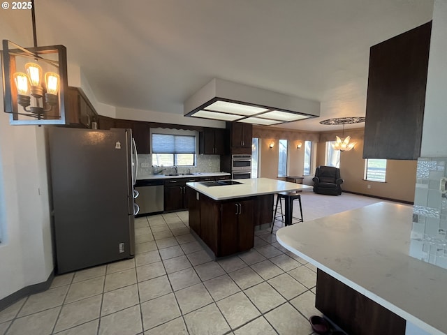 kitchen featuring open floor plan, light countertops, dark brown cabinets, a kitchen island, and stainless steel appliances
