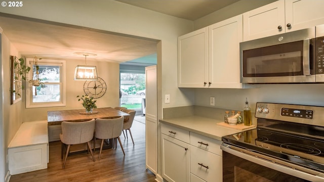 kitchen featuring dark wood-style floors, light countertops, hanging light fixtures, appliances with stainless steel finishes, and white cabinetry