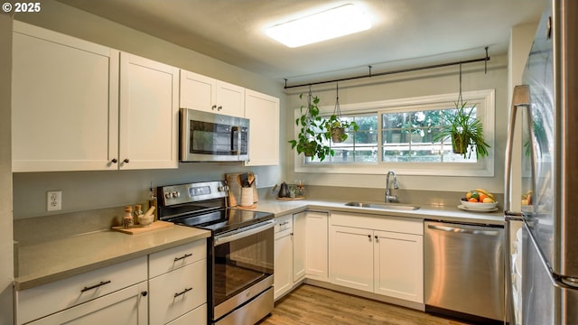 kitchen featuring white cabinets, appliances with stainless steel finishes, light countertops, light wood-style floors, and a sink