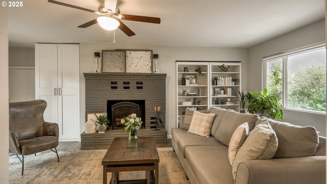 living area featuring a brick fireplace, a ceiling fan, and wood finished floors