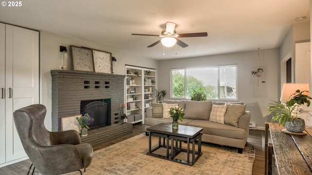 living area featuring a ceiling fan, a baseboard radiator, a brick fireplace, and wood finished floors