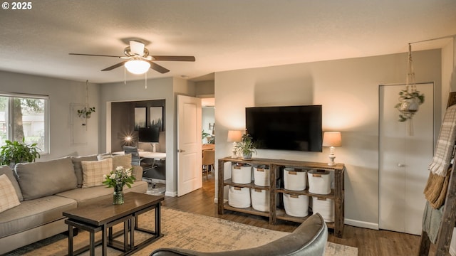 living area with wood finished floors, a ceiling fan, and baseboards