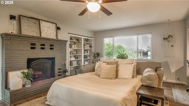 bedroom with a fireplace with raised hearth, ceiling fan, baseboards, and wood finished floors