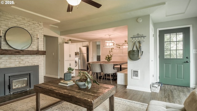 living room with washer / dryer, baseboards, wood finished floors, heating unit, and a fireplace