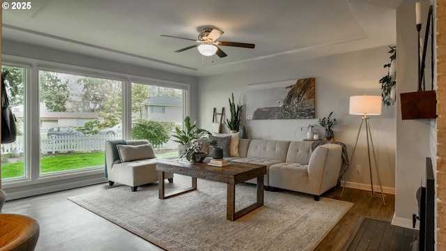 living area with a fireplace, wood finished floors, a ceiling fan, and baseboards