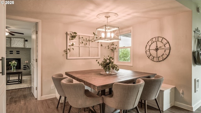 dining space with dark wood-type flooring, a fireplace with raised hearth, baseboards, and a ceiling fan