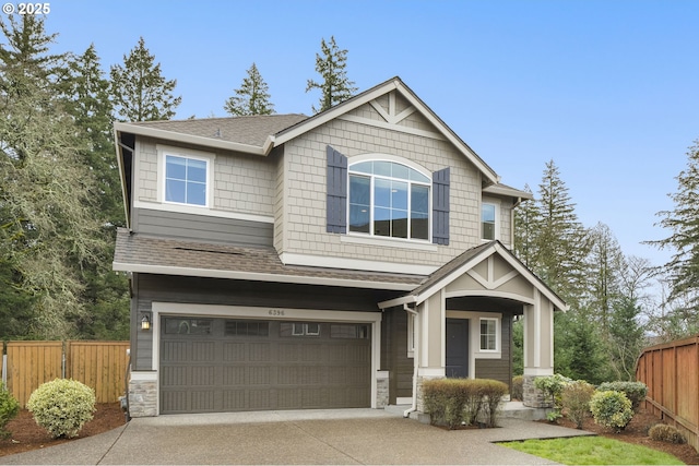 craftsman-style home with concrete driveway, an attached garage, fence, and stone siding