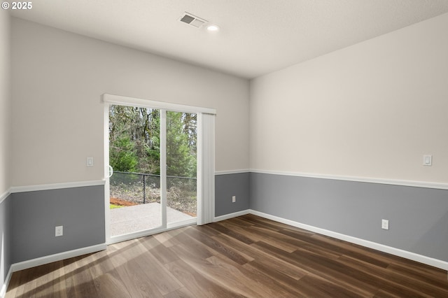 empty room featuring dark wood-style floors, visible vents, and baseboards