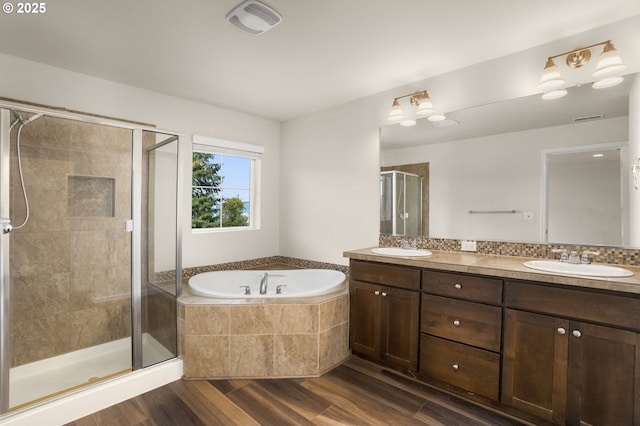 bathroom featuring wood finished floors, double vanity, a stall shower, a sink, and a garden tub