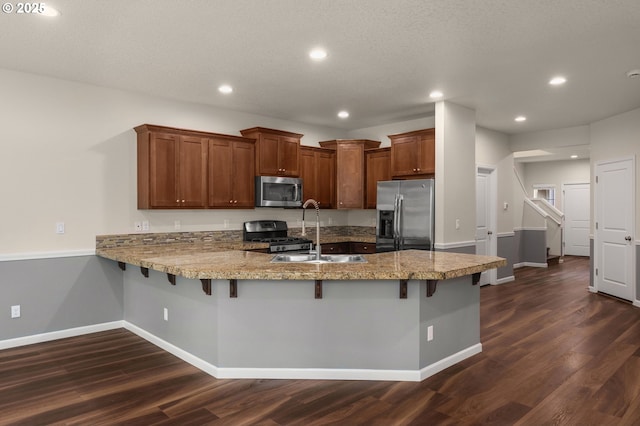 kitchen with a sink, appliances with stainless steel finishes, a peninsula, and dark wood-style flooring