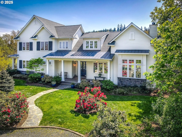 view of front of home featuring a front yard, a standing seam roof, roof with shingles, and covered porch