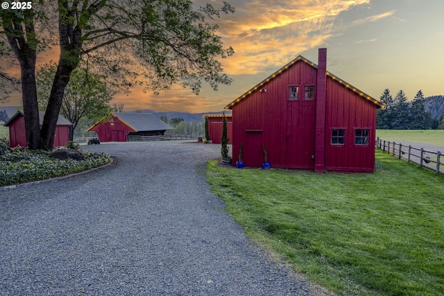 outdoor structure at dusk with a yard, an outbuilding, and fence