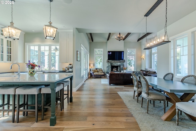 dining area featuring a stone fireplace, a wealth of natural light, a notable chandelier, and light wood-style floors