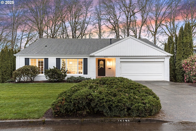 ranch-style house with a lawn, driveway, a shingled roof, a garage, and brick siding