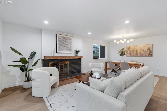 living area featuring wood finished floors, baseboards, recessed lighting, a brick fireplace, and a notable chandelier