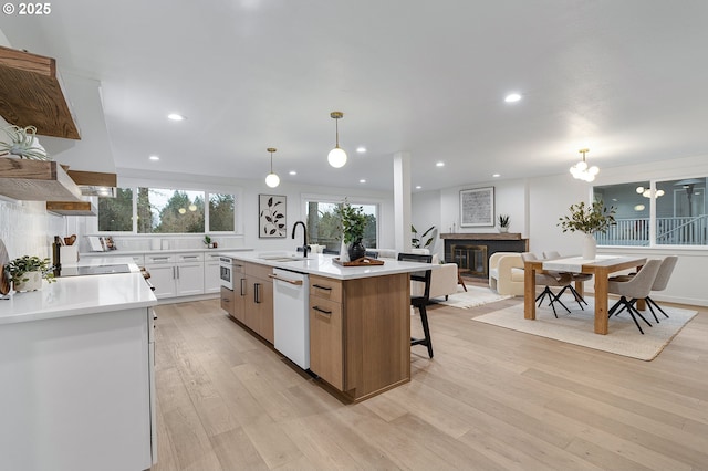 kitchen featuring a center island with sink, dishwasher, light countertops, light wood-style flooring, and a sink