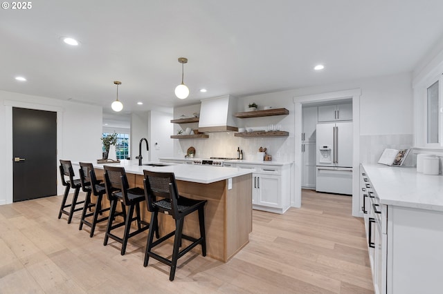 kitchen with open shelves, light wood-style floors, white fridge with ice dispenser, custom exhaust hood, and a sink