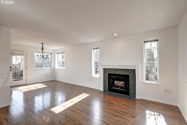 unfurnished living room featuring a chandelier, a fireplace, baseboards, and wood finished floors