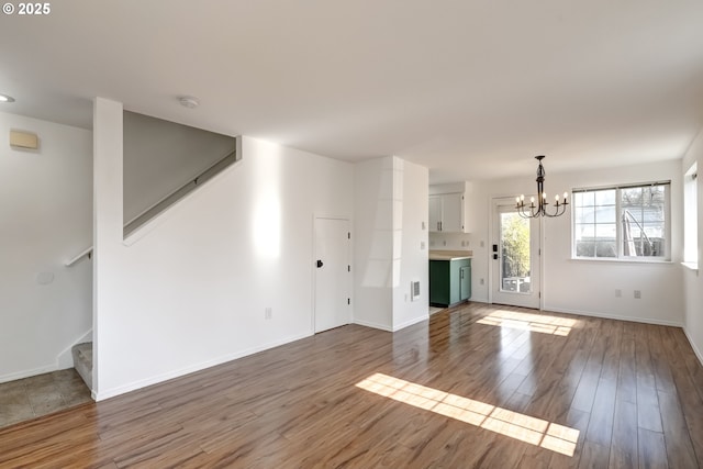 unfurnished living room featuring stairway, wood finished floors, visible vents, baseboards, and a chandelier