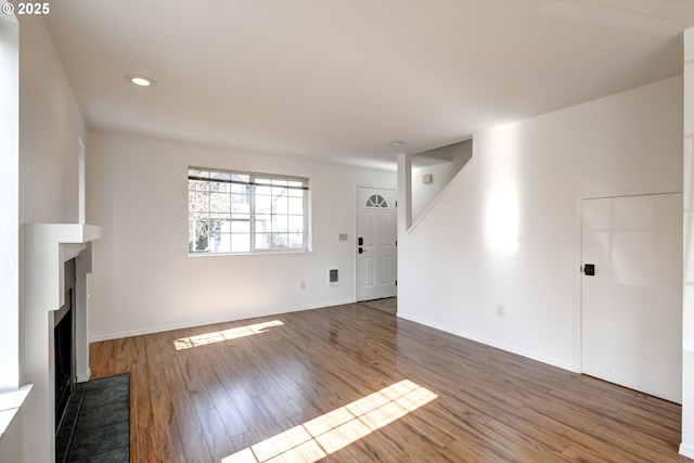 unfurnished living room with wood finished floors, recessed lighting, stairway, a fireplace, and baseboards