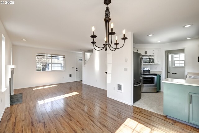 kitchen with light wood finished floors, decorative light fixtures, open floor plan, stainless steel appliances, and light countertops