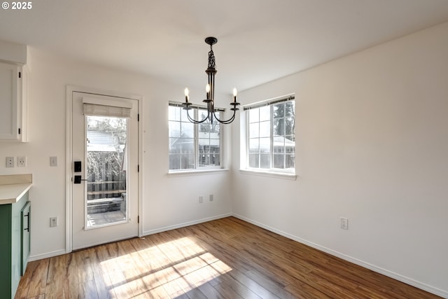 unfurnished dining area with baseboards, wood-type flooring, and a notable chandelier