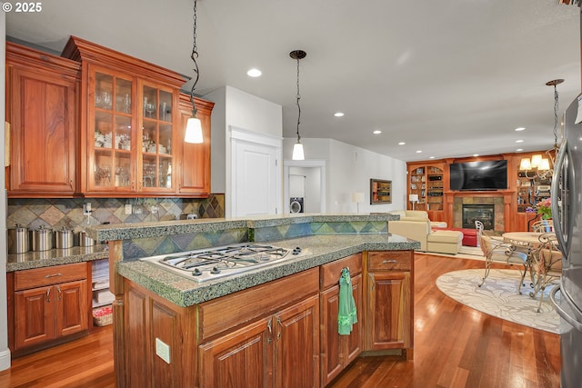 9459 SE Tarnahan Dr, Happy Valley, OR 97086 - kitchen with stainless steel appliances, a glass covered fireplace, dark wood finished floors, decorative backsplash, and glass insert cabinets
