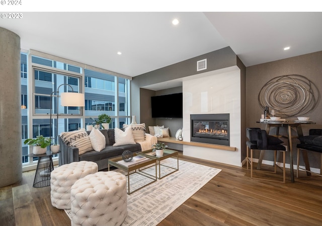 living area with visible vents, expansive windows, a glass covered fireplace, wood finished floors, and baseboards