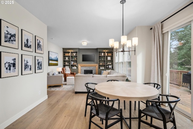 dining area with built in shelves, a stone fireplace, a chandelier, and light wood-type flooring