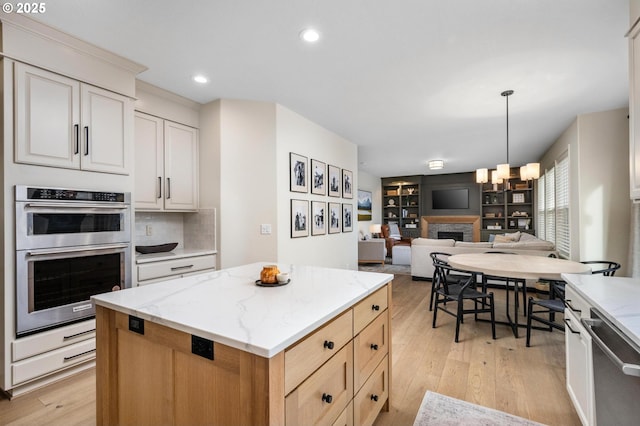 kitchen featuring white cabinets, hanging light fixtures, a kitchen island, light stone counters, and stainless steel appliances