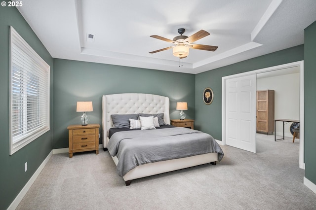 carpeted bedroom with a tray ceiling, ceiling fan, and a closet