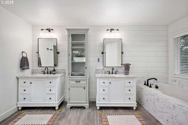 bathroom featuring hardwood / wood-style floors, vanity, a textured ceiling, and tiled tub