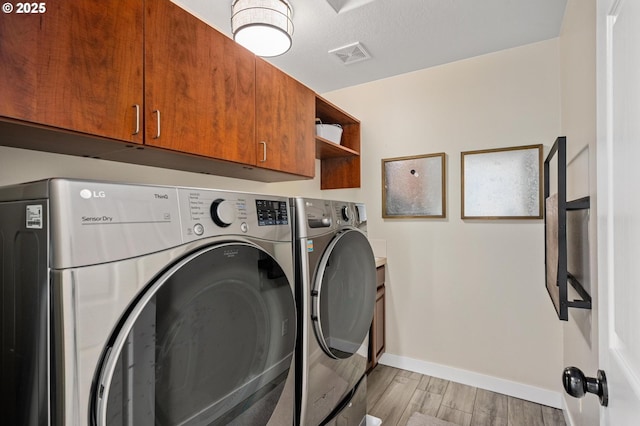 clothes washing area with cabinets, washing machine and dryer, and light hardwood / wood-style flooring