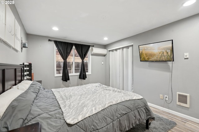 bedroom with heating unit, an AC wall unit, and light wood-type flooring