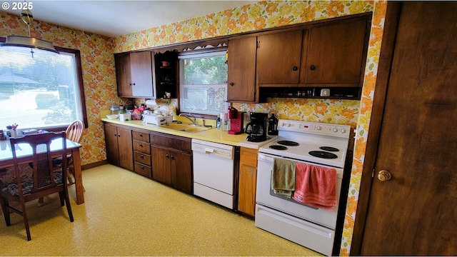 kitchen featuring a sink, wallpapered walls, white appliances, light countertops, and light floors