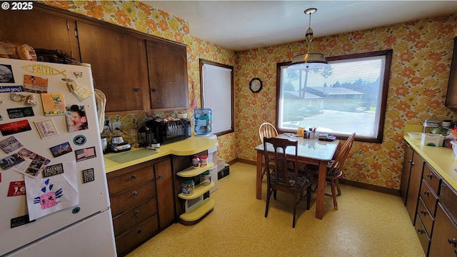 kitchen featuring wallpapered walls, baseboards, light countertops, and freestanding refrigerator