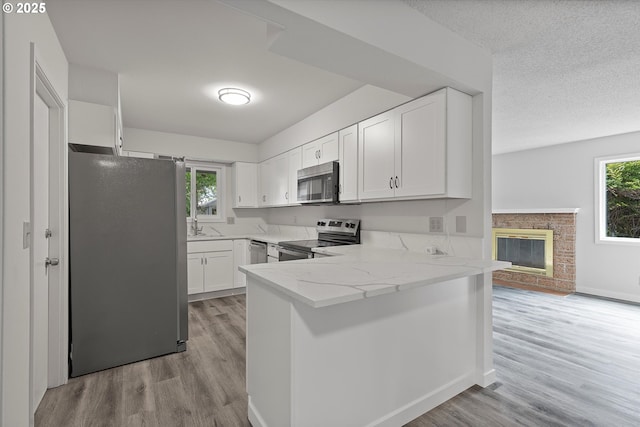 245 NE 4th Ave, Hillsboro, OR 97124 - kitchen featuring stainless steel appliances, a peninsula, healthy amount of natural light, light wood-type flooring, and a textured ceiling
