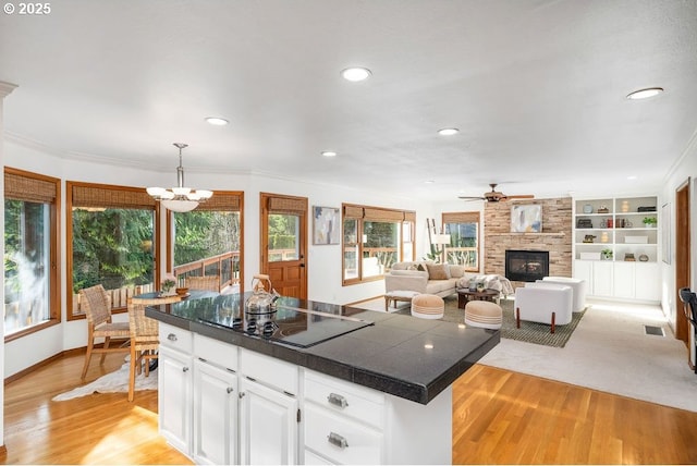 kitchen with black electric stovetop, light wood-type flooring, a fireplace, white cabinetry, and hanging light fixtures