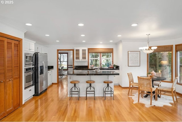 kitchen with appliances with stainless steel finishes, pendant lighting, light hardwood / wood-style flooring, a notable chandelier, and white cabinets