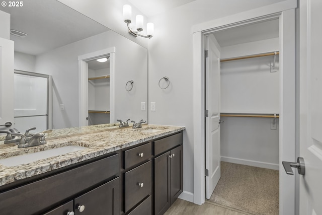 bathroom with a shower with shower door, a sink, baseboards, and double vanity