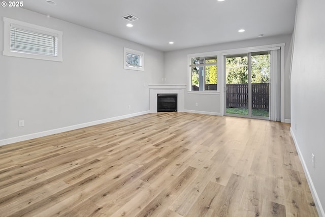 unfurnished living room with a glass covered fireplace, visible vents, light wood-style flooring, and baseboards