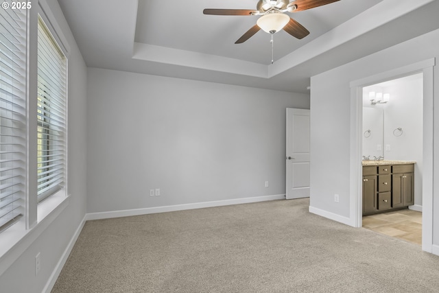 unfurnished bedroom with a raised ceiling, light colored carpet, ensuite bathroom, a sink, and baseboards