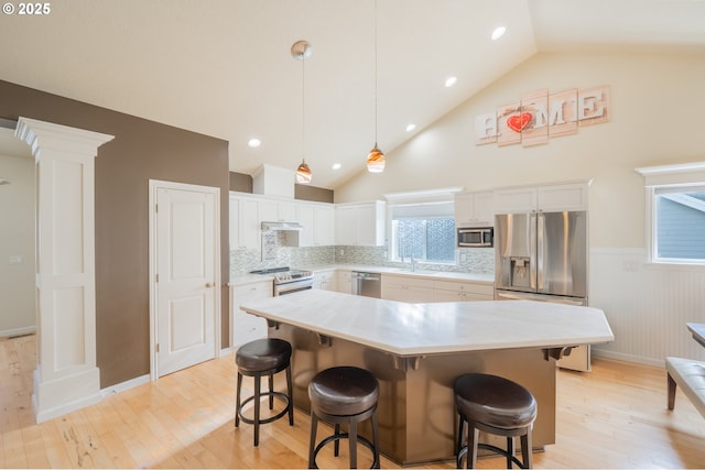 kitchen featuring stainless steel appliances, light wood-style floors, wainscoting, a sink, and ornate columns