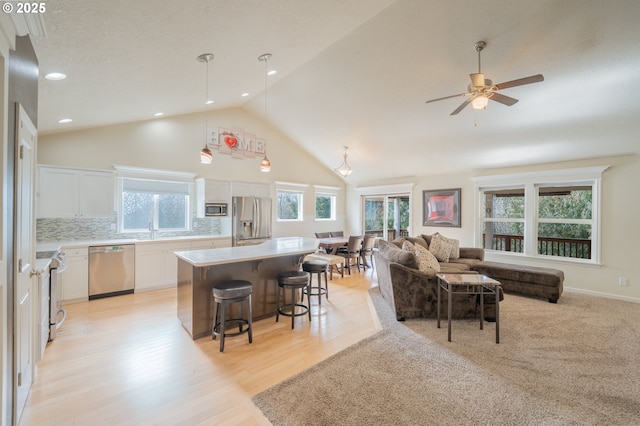 kitchen featuring a breakfast bar area, stainless steel appliances, decorative backsplash, open floor plan, and white cabinetry