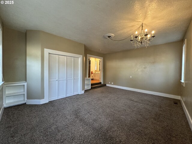 212 NW Bridge St, John Day, OR 97845 - unfurnished bedroom with a textured ceiling, a chandelier, dark carpet, and baseboards