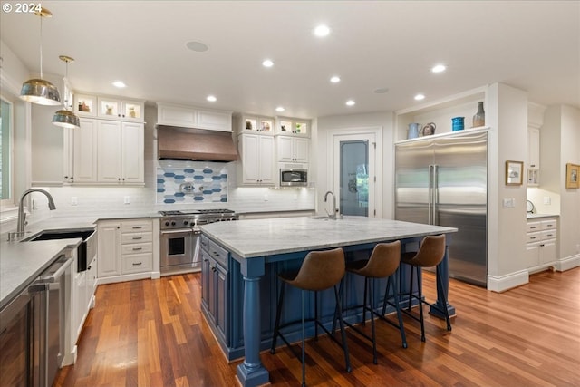 kitchen with white cabinets, light stone countertops, an island with sink, and built in appliances