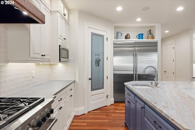 kitchen with exhaust hood, light stone countertops, blue cabinetry, white cabinets, and high quality appliances