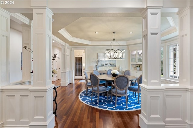 dining room featuring a raised ceiling, an inviting chandelier, crown molding, dark hardwood / wood-style flooring, and decorative columns