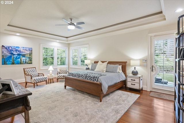 bedroom featuring ceiling fan, wood-type flooring, crown molding, and a tray ceiling