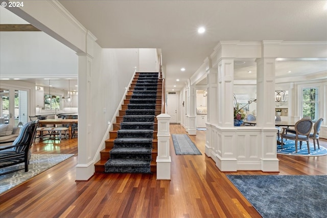 staircase featuring ornate columns, crown molding, and wood-type flooring